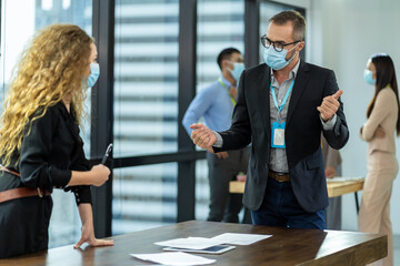 Business man and business woman wearing protective medical face mask, wearing formal suite, sitting and working with computer laptop in the modern office. health, businesspeople and office concept