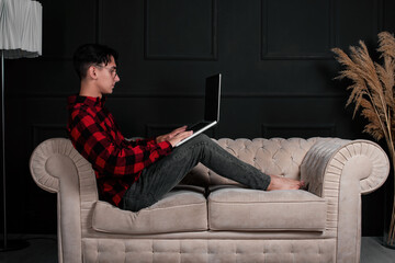 An intelligent and handsome student learns remotely at home while lying on the couch. Online lecture on laptop. The copywriter works outside the office.