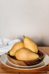 Three organic pears in wooden plate on wooden table.