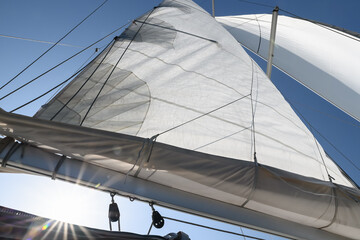 Sun rays through sails, cables, ropes and slats. Bottom up view on clear blue sky