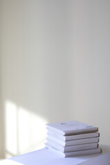 White stacked books on a shelf minimalist vertical photography with copy space and sunlight on the wall. 