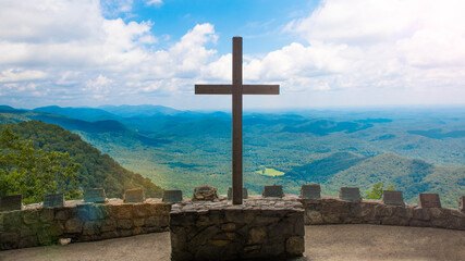 Cross. Wooden Cross on rock stand. Religious symbol. Christian or Baptist church. Faith in Jesus Christ. Mountains landscape, blue sky, clouds and sunlight on background.