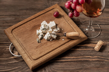 Blue cheese, wine in a glass and a bunch of grapes on a wooden board. Concept for wine and cheese...