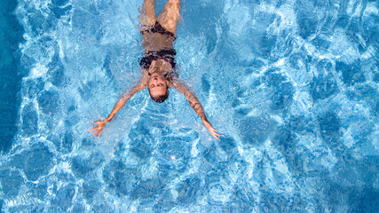 Active young girl in swimming pool aerial drone view from above, young woman swims in blue water pool, tropical vacation on holiday resort 
