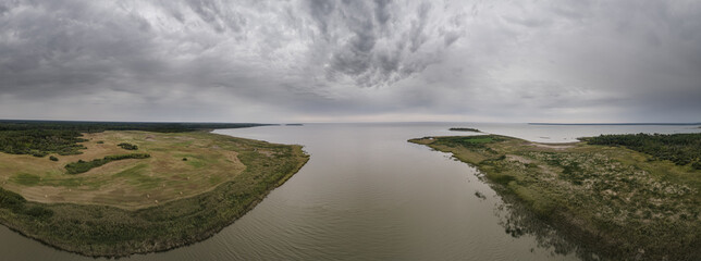 Aerial view of a large river and distant lake surrounded by mash and farm fields under a grey sky filled with clouds.

