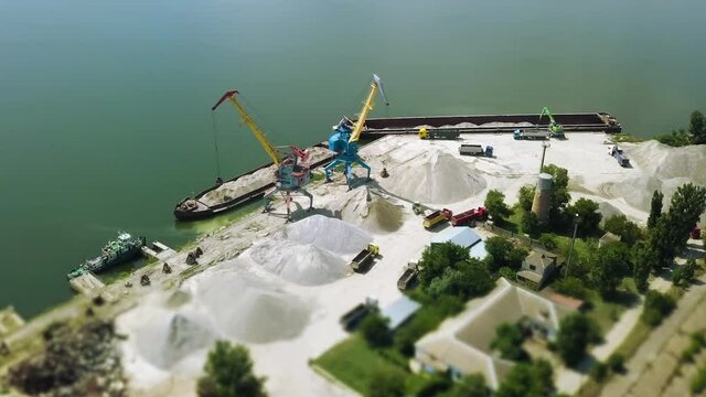 River Harbour with Working Cranes and Trucks Full of Crushed Stone Gravel Loaded From Barges Wherries with Tilt Shift Effect Filming from Drone Aerial View. Bulk Carrier Working Unloading