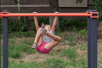Obraz premium cheerful funny naughty girl 6-7 years old plays on the playground and hangs on the uneven bars