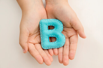 Stuffed felt letter of the alphabet in open hands of child. Kid holding handmade capital letter 