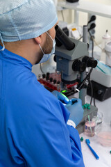 Naklejka na ściany i meble A male scientist in a mask looks through a microscope in a laboratory.