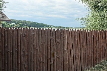 Fototapeta premium long brown wooden wall of a fence made of planks in a palisade on the street against a gray sky