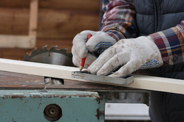 A man using a carpenter's square and a pencil makes markings on a wooden block