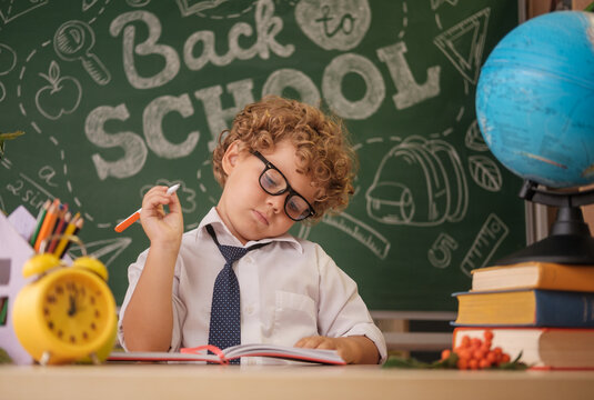 a cute curly-haired boy is sitting at a desk against the background of a blackboard with the inscription in English back to school
