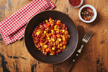 Chili Con Carne with ground beef, beans and corn in dark bowl on wooden background. Mexican and Texas cuisine