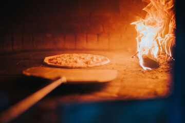 Closeup of a pizza with an oven peel in the masonry oven of a restaurant