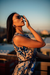 Close up image of happy brunette woman in sunglasses and summer clothes posing sideways outdoors