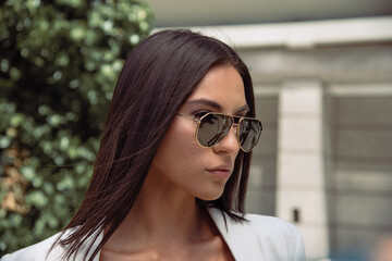 Close up image of happy brunette woman in sunglasses and summer clothes posing sideways outdoors
