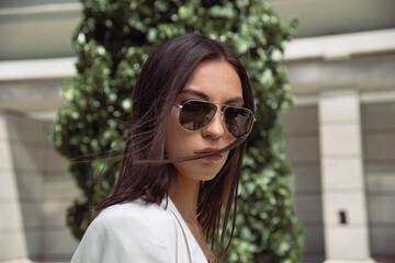Close up image of happy brunette woman in sunglasses and summer clothes posing sideways outdoors