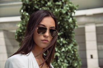Close up image of happy brunette woman in sunglasses and summer clothes posing sideways outdoors