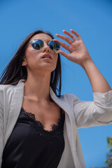 Close up image of happy brunette woman in sunglasses and summer clothes posing sideways outdoors