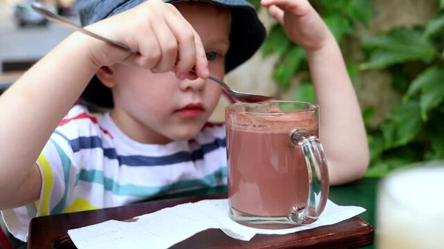 Little cute happy smiling boy drinking cacao cocktail smiling looking at screen making funny face. Traveling family urban lifestyle. Emotional male child enjoying free time outside. Kids enjoyment. 