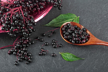 Raw ripe elderberry in a bowl with green leaves on a black stone table. European black elderberry. Sambucus nigra.