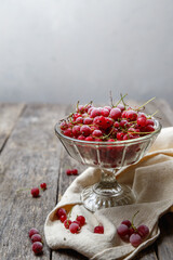 Frozen red currants in a glass vase on a cloth on a rustic wooden table. Close-up.