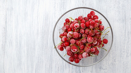 Frozen red currants in a glass vase on a white wooden table. Close-up.