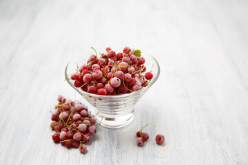 Frozen red currants in a glass vase on a white wooden table. Close-up.