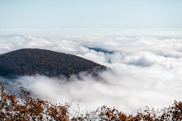 Clouds inversion fog at Devil's Knob Overlook at Wintergreen resort town in Blue Ridge parkway mountains with autumn fall foliage trees covering peak high angle view