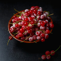 Frozen red currants in a brown ceramic vase on black background. Close-up.
