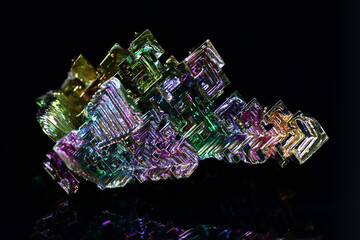 Synthetic bismuth (Bismuthum) crystal with iridescent oxide film on black background close up
