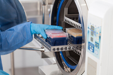 Young female scientist sterilizing laboratory material in autoclave