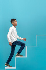 Young smiling teen boy climbs the development ladder against blue background. Education concept