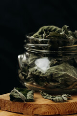 Dry mint leaf on in a glass jar on a wooden table against a black background. Jar with mint on a wooden table. Mint for medicinal tea.