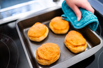 Fresh baked tray serving of buttermilk biscuits food with hand and oven mitt after baking for morning traditional southern breakfast