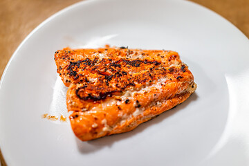 Grilled baked or fried sockeye salmon seafood fish closeup above with red color and omega 3 nutrition on white plate with black pepper seasoning