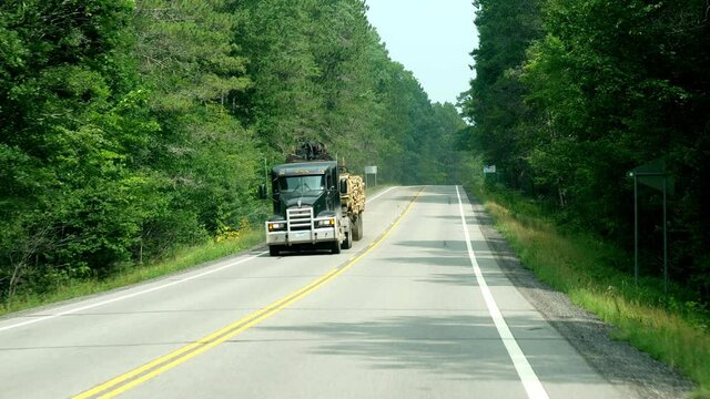 CASS CO, MN - 6 AUG 2021: Two clips of semi trailer trucks on a forest lined highway in Minnesota. Slow motion of flatbed haulers, through a windshield.
