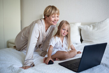 little girl with her grandmother sitting on the bed in front of a laptop
