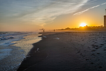 Colorful sunset at Myrtle Beach city by Atlantic ocean with sun behind horizon by condo condominium apartment buildings, people silhouettes walking by crashing waves in resort South Carolina town