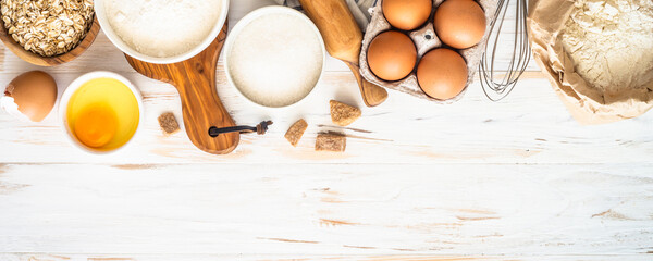 Baking ingredients. Flour, sugar, egg and rolling pin at white wooden table. Long banner format.