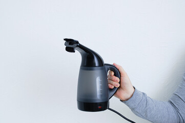 Handheld garment steamer in the hand of caucasian woman. White background.