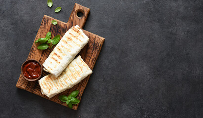 Shawarma with meat and vegetables on a wooden board on a black background, top view.