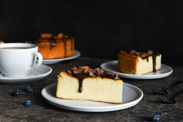 Cheesecake new york. Slice cheesecake with chocolate sauce and a cup of coffee on a dark concrete background.