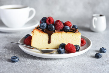 slice of cheesecake with chocolate sauce, berries and a cup of coffee on the kitchen table, on a concrete background.