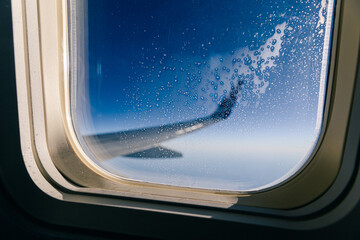 Looking out of airplane porthole. Focus on window frost. Plane wing out of focus in background.