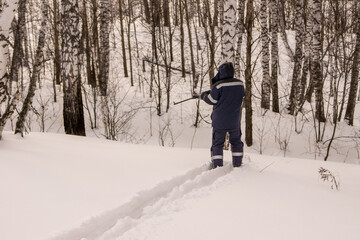 man is standing on skis in the forest and aiming his weapon down the ravine. A hunter or poacher...