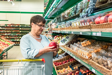 An elderly woman chooses fruits in the store. Grandma in the fruit section of the supermarket.