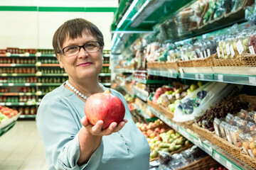 An elderly woman chooses fruits in the store. Grandma in the fruit section of the supermarket.