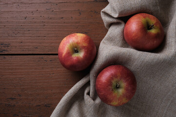 Fruits in a linen tablecloth on a old wooden table. Apples on a dark red background. Place for text.