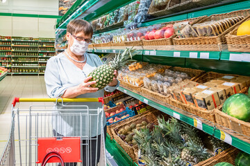 Obraz premium Grandma holds pineapples in her hand in the grocery section of the supermarket.